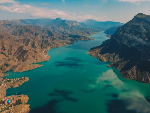 Free Stunning aerial capture of a serene mountain lake, with clear blue water reflecting the sky and surrounding mountains. Stock Photo