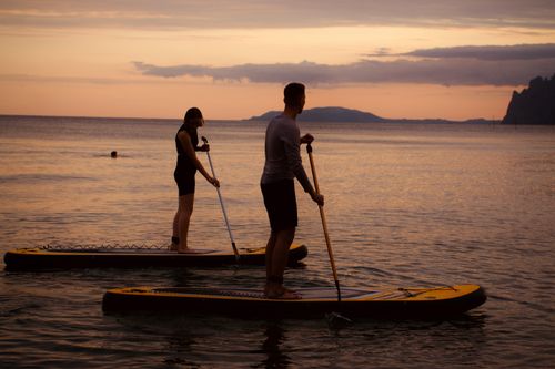 Free A couple enjoys paddleboarding during a beautiful sunset on the ocean, showcasing water-based adventure. Stock Photo