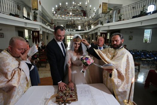 Bride and groom in a traditional wedding ceremony with priests in an ornate church.