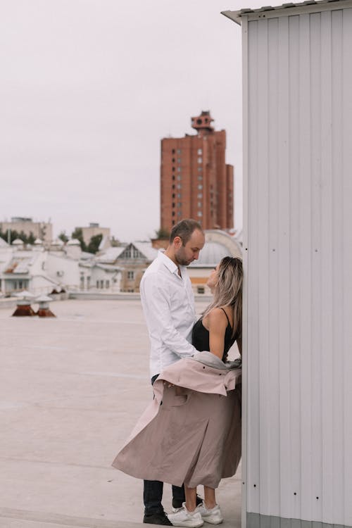 Man in White Shirt Hugging Woman in Black Tank Top and Beige Trench Coat on the Rooftop