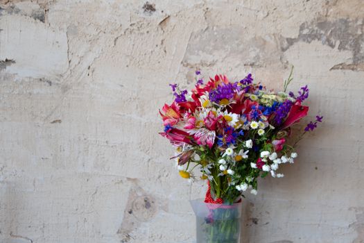 Colorful wildflower bouquet in a vase against a rustic beige wall, perfect for summer decor.