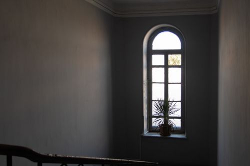 Free A dimly lit interior stairway with an arched window and a potted plant, conveying a minimalist aesthetic. Stock Photo