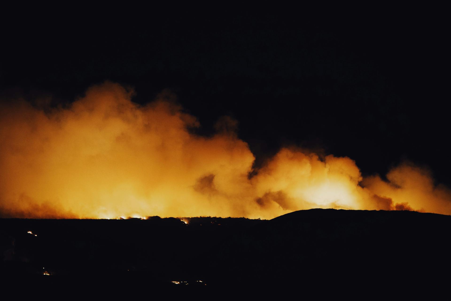 A powerful nighttime image of a wildfire with glowing flames and rising smoke, capturing the intensity of nature's fury.