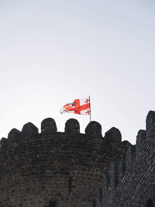 Free A historic castle tower with Georgia's national flag fluttering in the sky. Stock Photo
