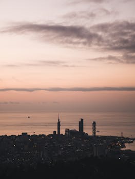A stunning aerial view of a city skyline at dusk with cloudy skies and an ocean backdrop.