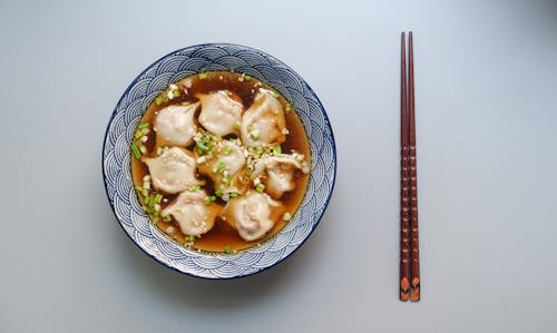 免费 圆形的白色和蓝色陶瓷碗配煮熟的球汤和棕色木筷子 素材图片