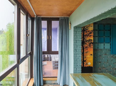 Bright modern interior featuring floor-to-ceiling glass windows, blue curtains, and artistic decor.