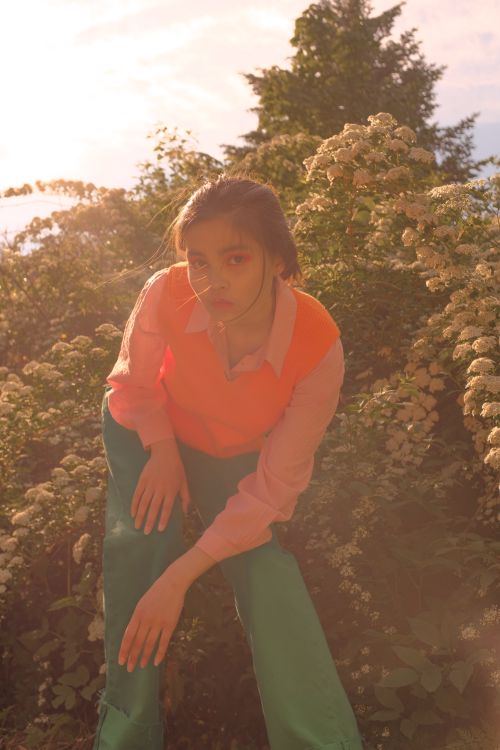 Free Stylish woman in bright outfit posing amid blooming shrubs in sunlit garden. Stock Photo