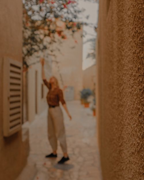 Free A woman reaches up to touch flowers in a tranquil, charming alleyway. Stock Photo