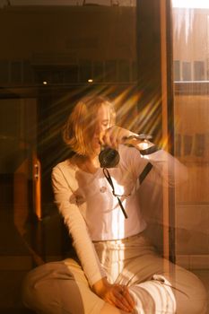 Woman in white long sleeves capturing a moment with a camera through a sunlit window reflection.