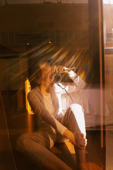 Artistic reflection of a woman taking a photo indoors with sunlight streaming through.
