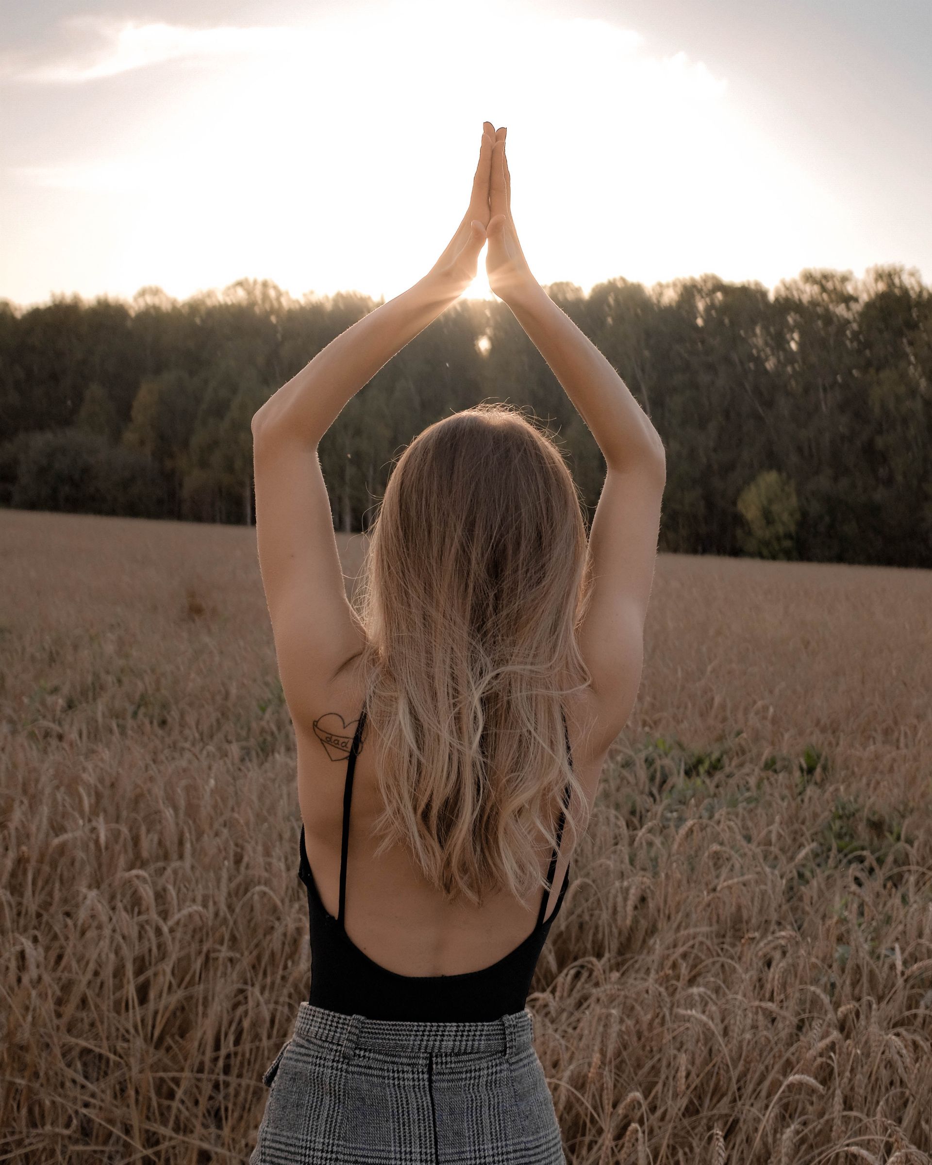 Woman standing back-facing in open field at golden hour