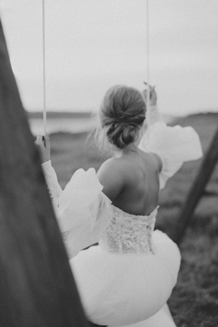 A Bride In Wedding Gown Sitting On The Swing