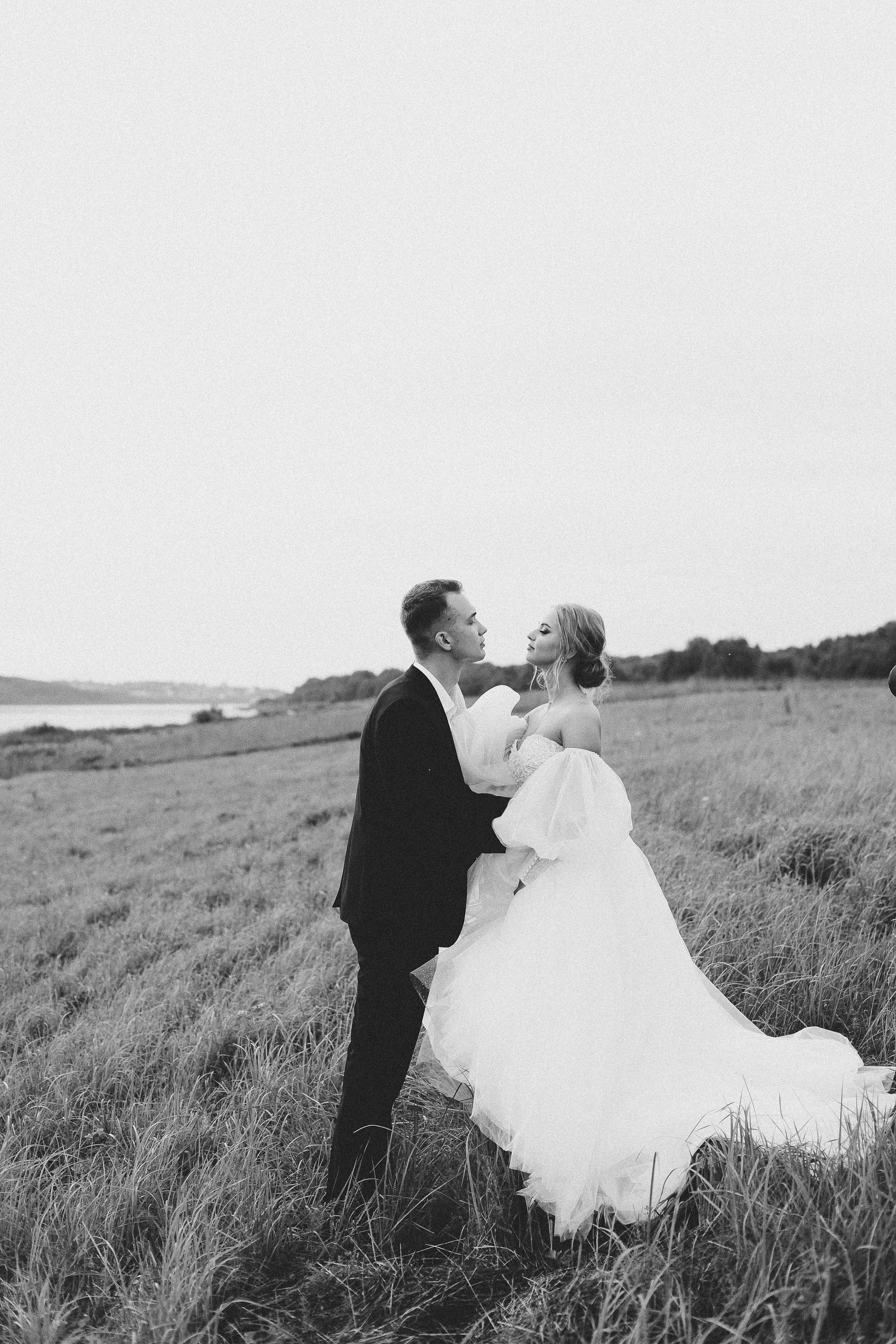 Black and white portrait of a bride and groom embracing in a serene grassy field, capturing love.