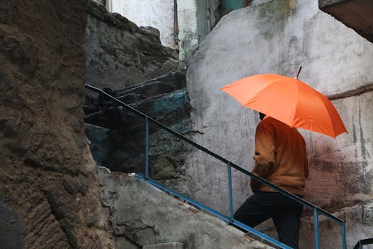 A person climbs weathered stone stairs with an orange umbrella in a rustic setting.