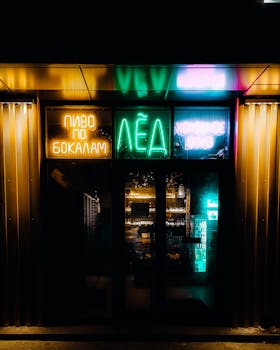 Colorful neon signage on shop entrance at night, displaying bright lights and reflections.