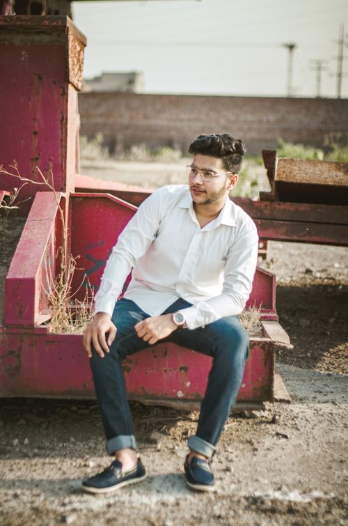 Free Young man in white shirt and jeans sitting outdoors on a sunny day. Stock Photo