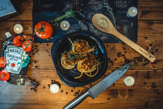 Top view of bolognese pasta with rustic elements on a wooden table, lit by candlelight.