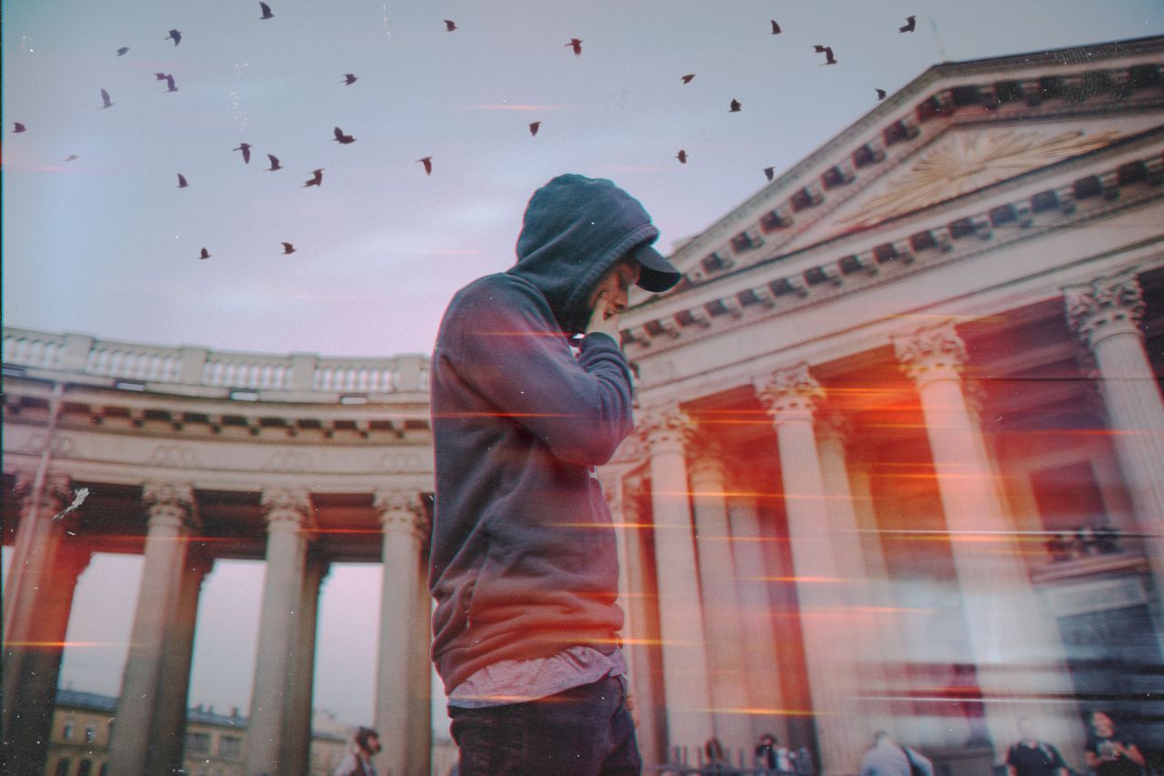 a man in a hoodie walks near a landmark building at twilight with bird