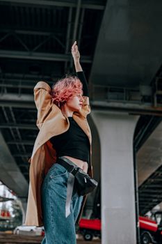 A trendy woman with dyed hair poses confidently under a bridge, embodying urban style.