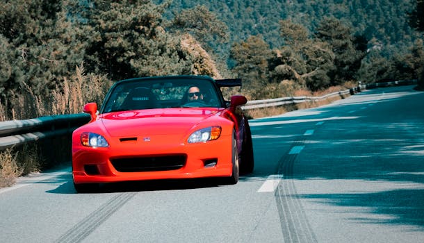 A vibrant red convertible speeds through a scenic mountain road in Sion, Switzerland, showcasing automotive elegance.
