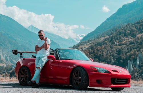 Free A Man Leaning on a Red Sports Car Stock Photo