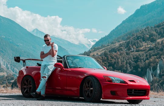 A man poses with a red convertible sports car against the backdrop of scenic Swiss mountains.