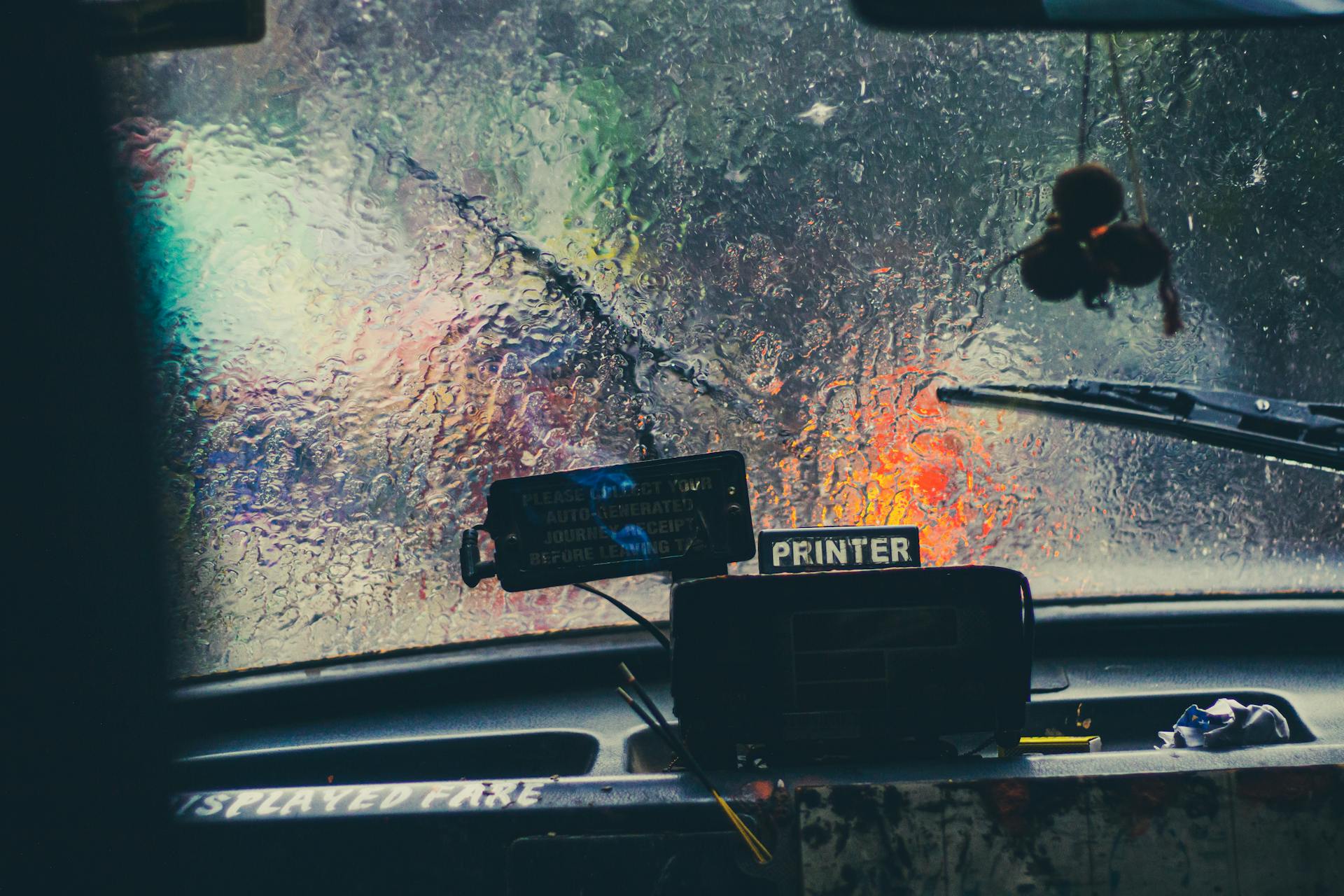 Blurry view through a rain-covered car windshield showcasing rainy weather and city lights.