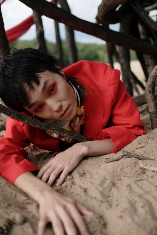 Free Person in vibrant red suit lying on sand among twisted branches, exuding a surreal artistic vibe. Stock Photo