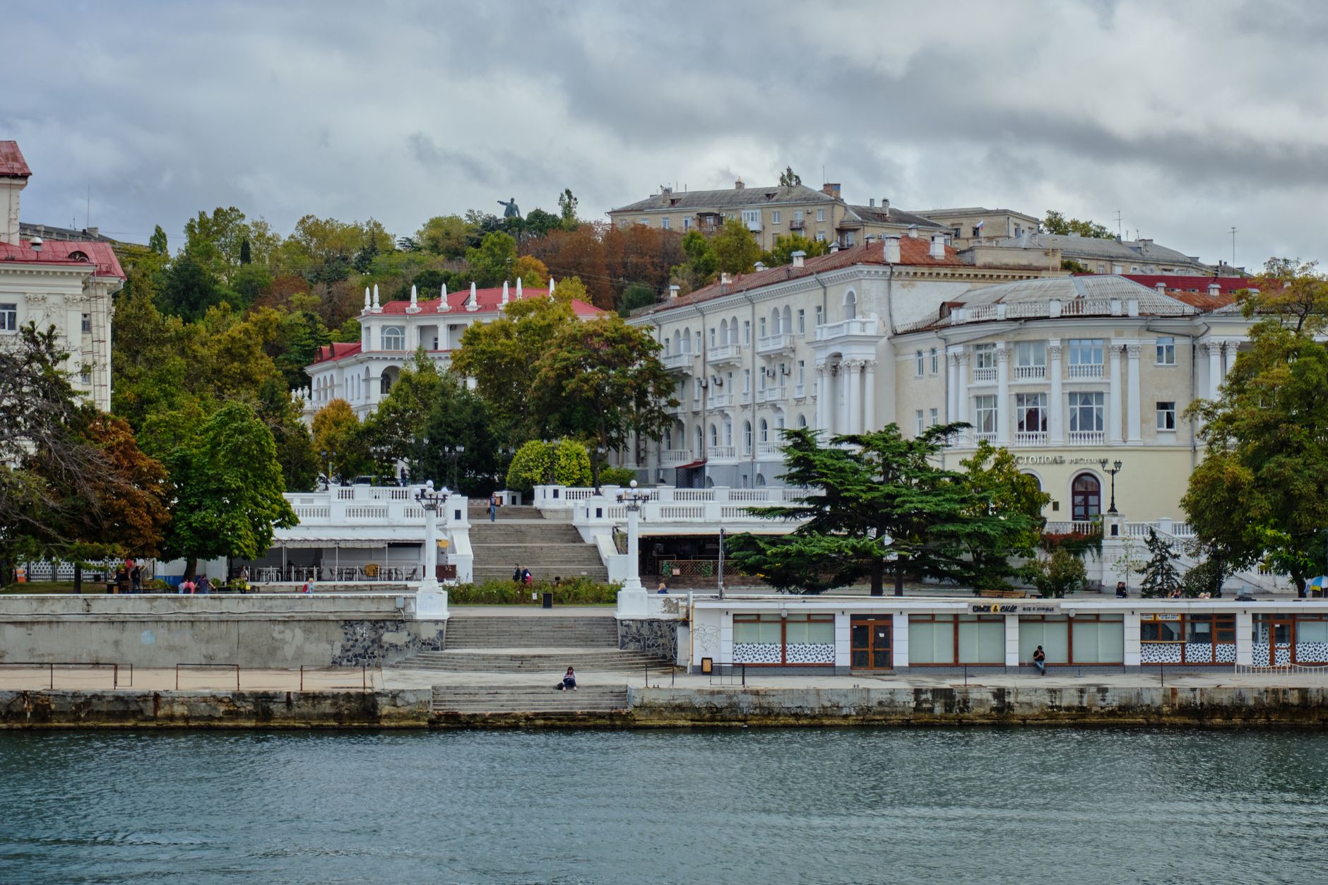 Scenic view of Sevastopol's waterfront architecture with lush autumn trees and a calm river reflecting buildings.