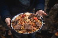 A flavorful plate of beef and rice pilaf with vegetables cooked outdoors, served with garnishes.
