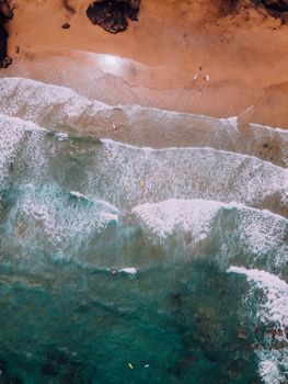 Stunning aerial shot of surfers riding waves on a sandy beach in Spain.