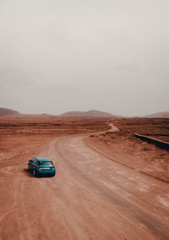 A blue car travels along a winding road through the sparse, desert landscape of Spain.