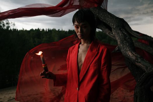 A person in a red suit holding a torch in a mysterious forest, creating an enigmatic atmosphere.