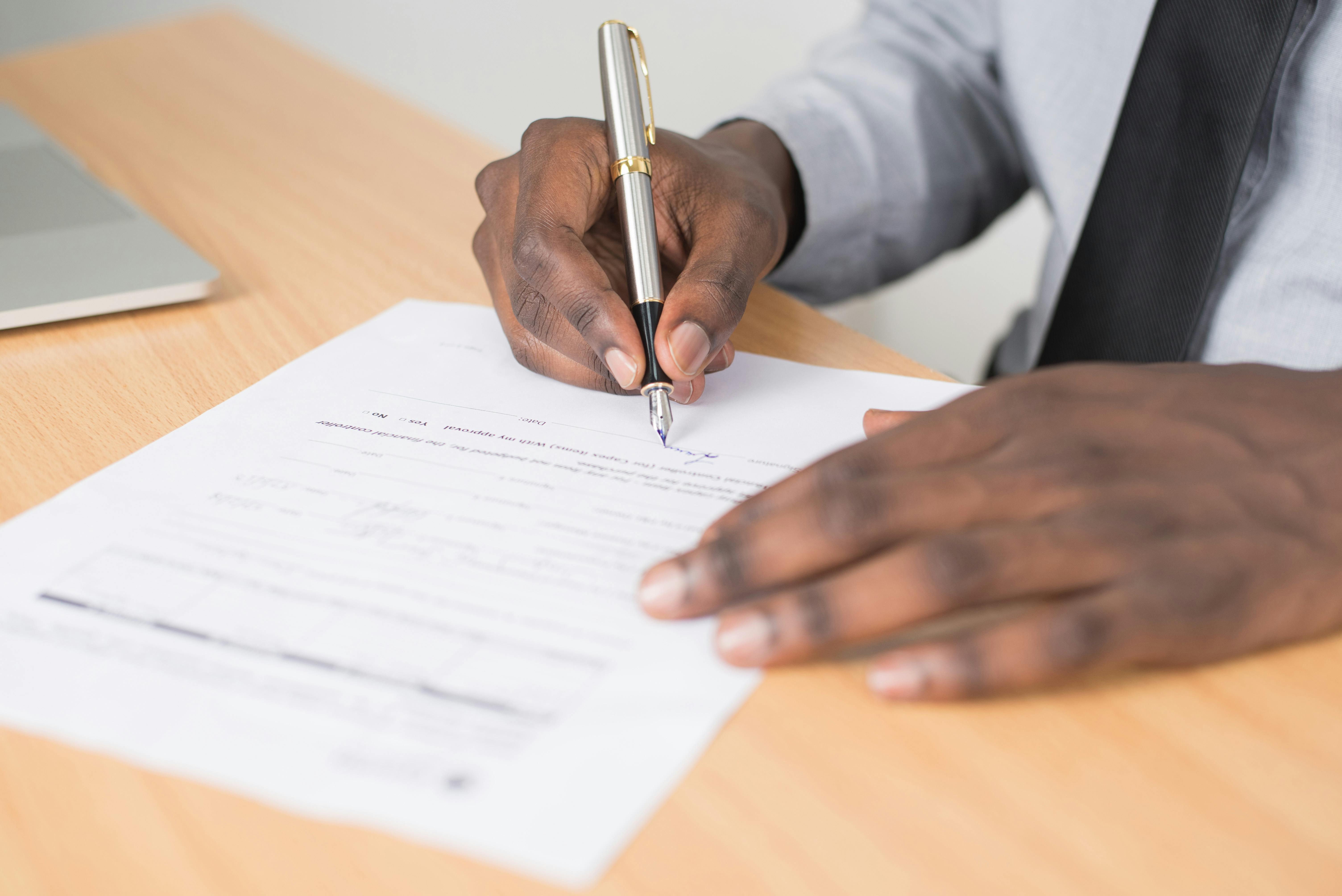 Free Person Holding Gray Twist Pen and White Printer Paper on Brown Wooden Table Stock Photo