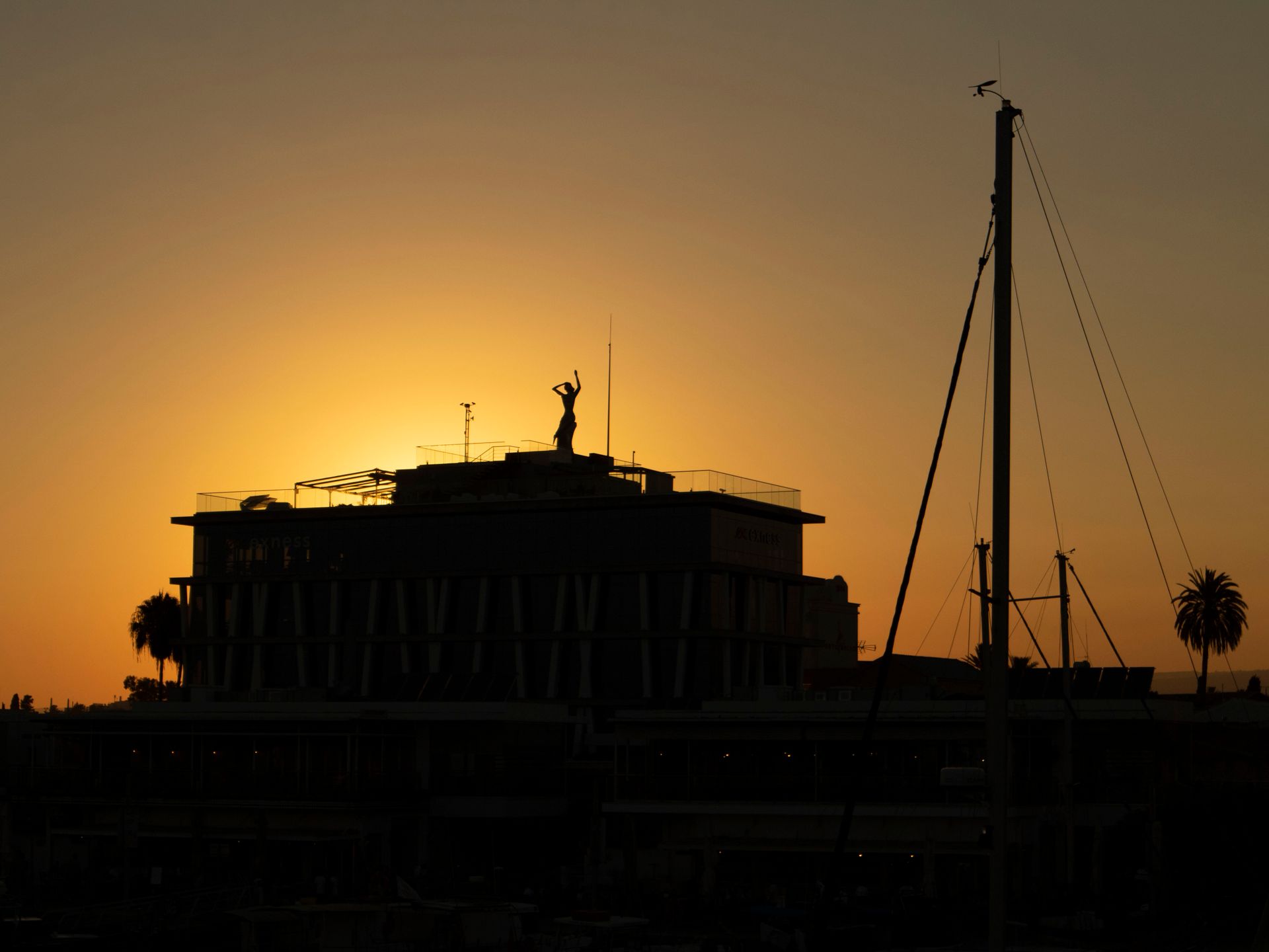 A striking silhouette of a building and sailboat mast against a vibrant sunset sky, depicting tranquility and beauty.