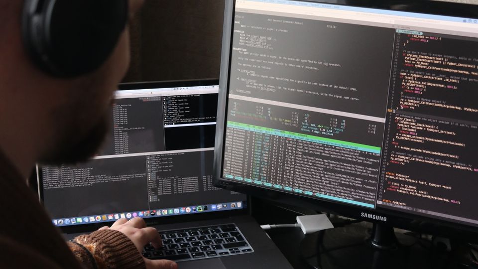 Pessoa desenvolvedora trabalhando com código em um computador e notebook.