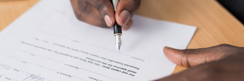 Close-up of a man's hands signing a formal document indoors.