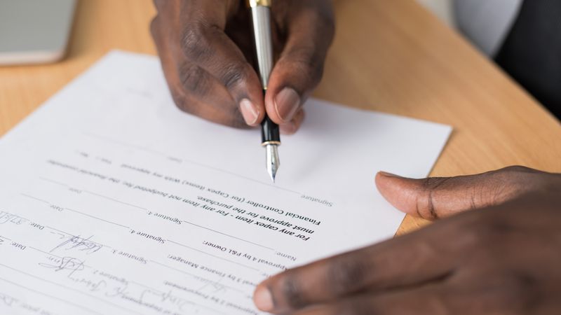 Close-up of a man's hands signing a formal document indoors.