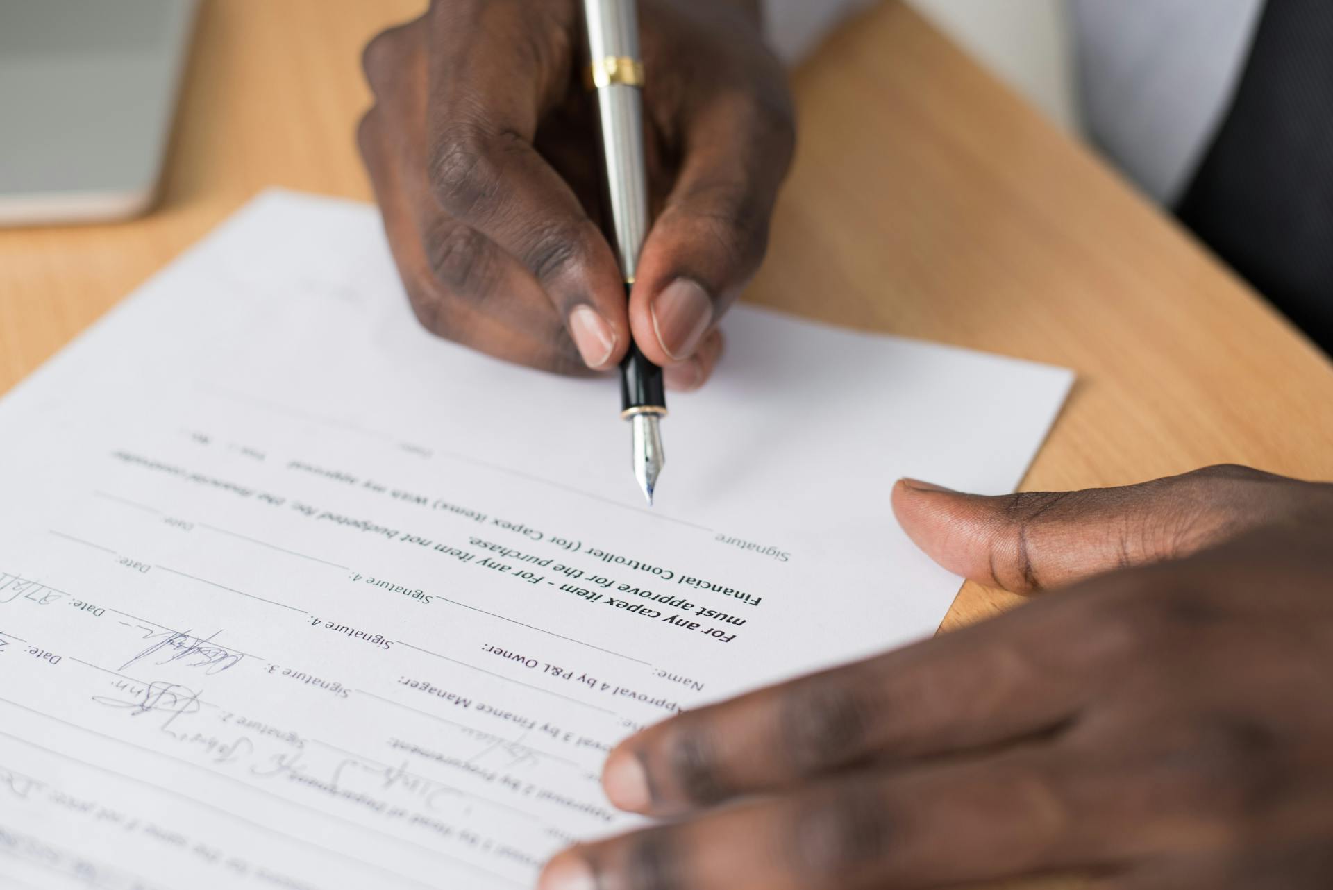 Close-up of a man's hands signing a formal document indoors.