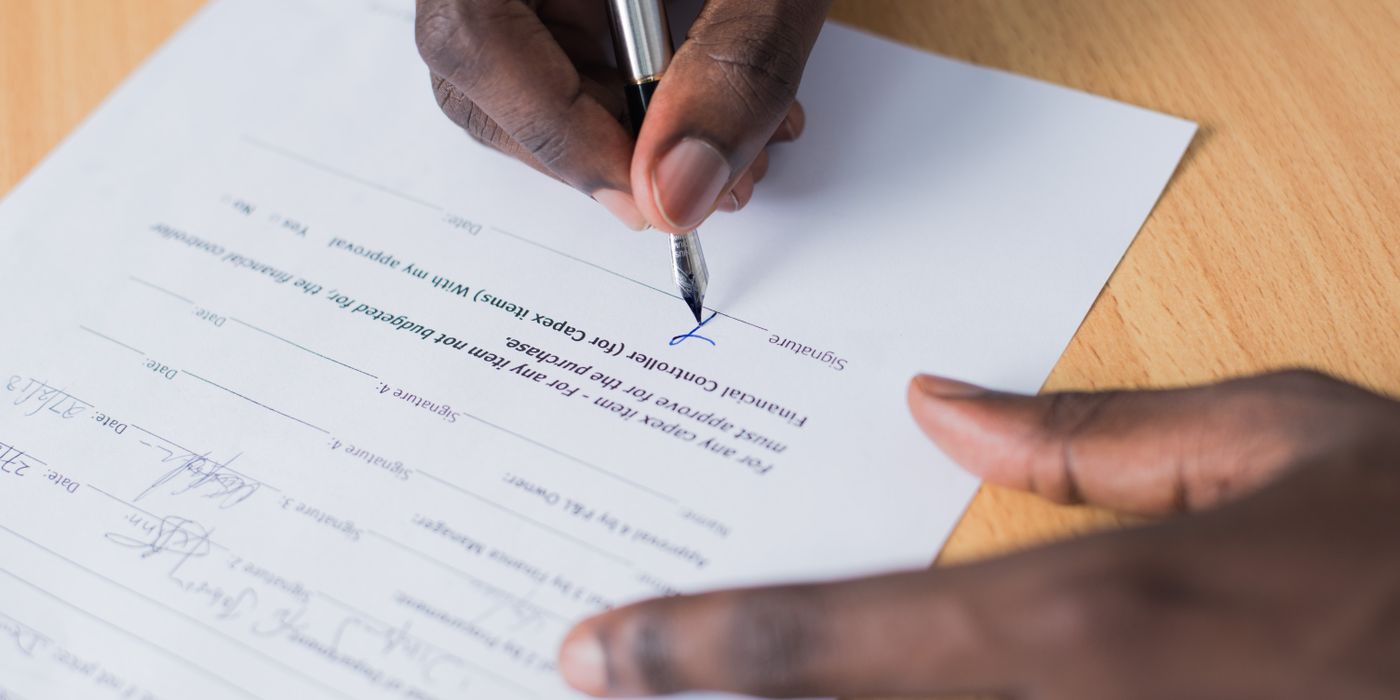 A close-up view of a person's hand signing a business contract on a desk with a pen.