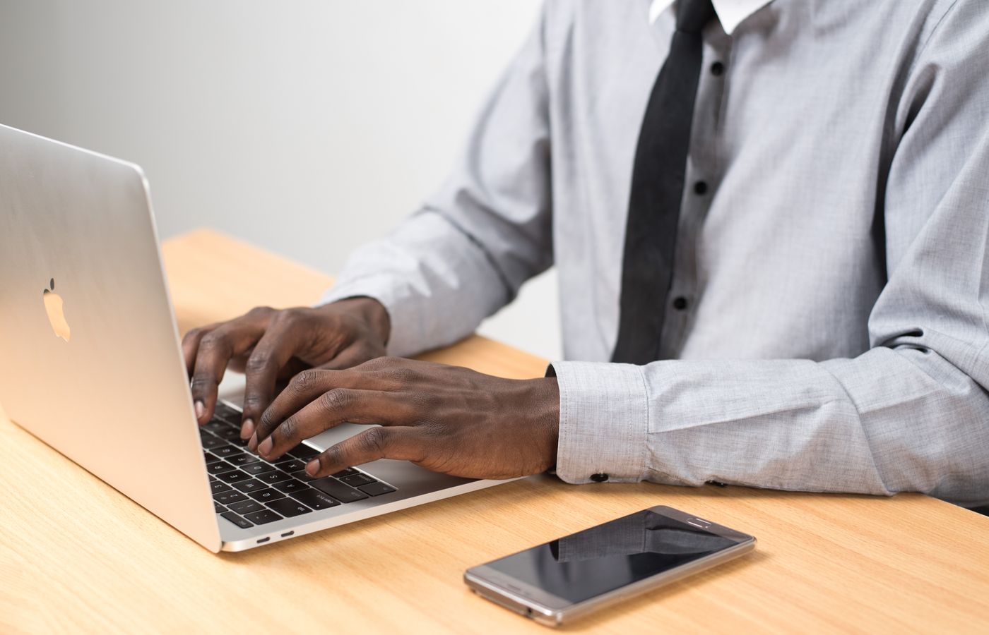 Businessman typing on a laptop in a modern office setting with a smartphone on the desk.