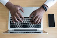 一个人正在笔记本电脑上打字，旁边放着智能手机，展现了现代技术的应用