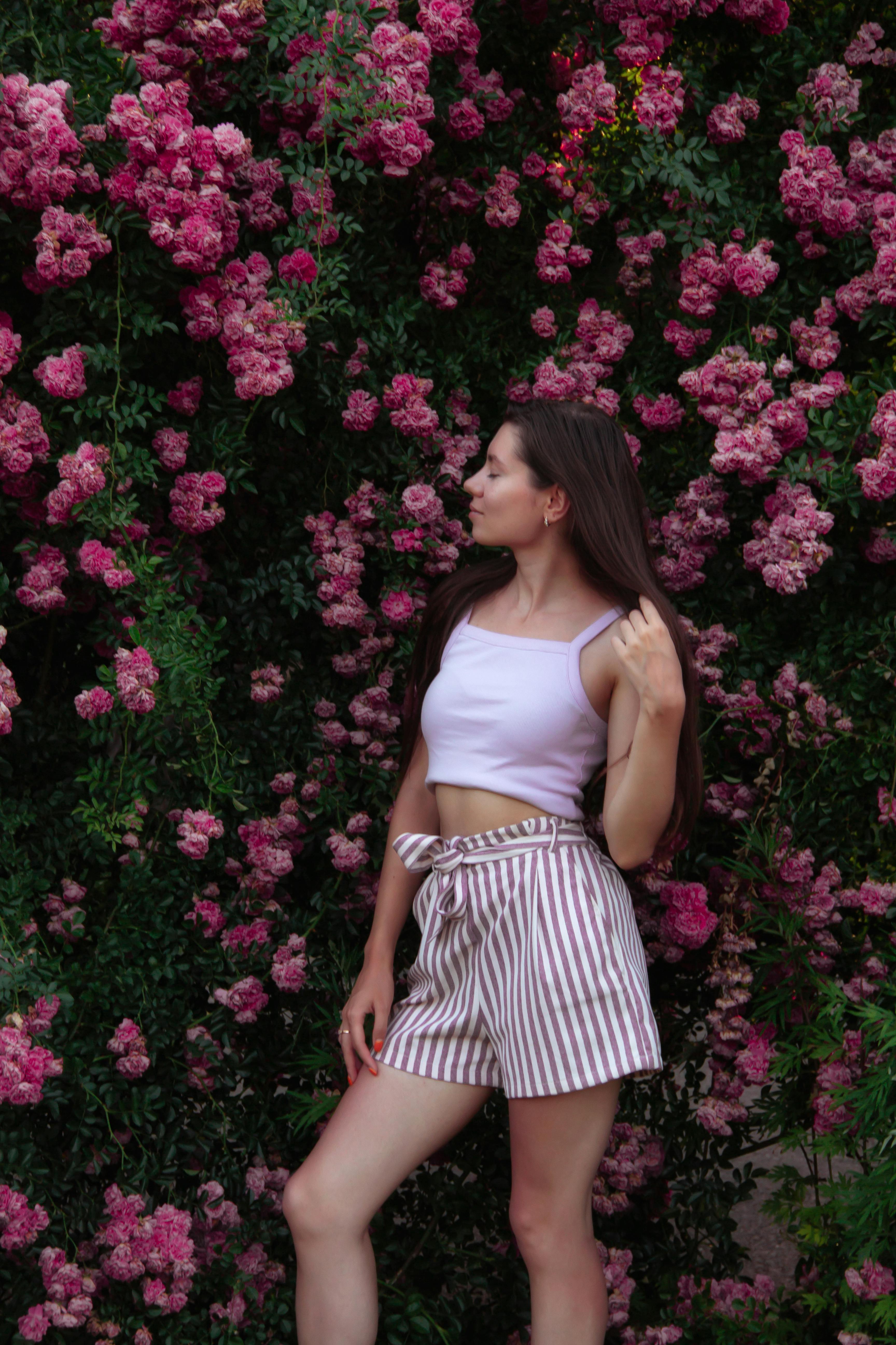 A young woman poses gracefully against a wall of vibrant pink roses, embracing the beauty of nature.