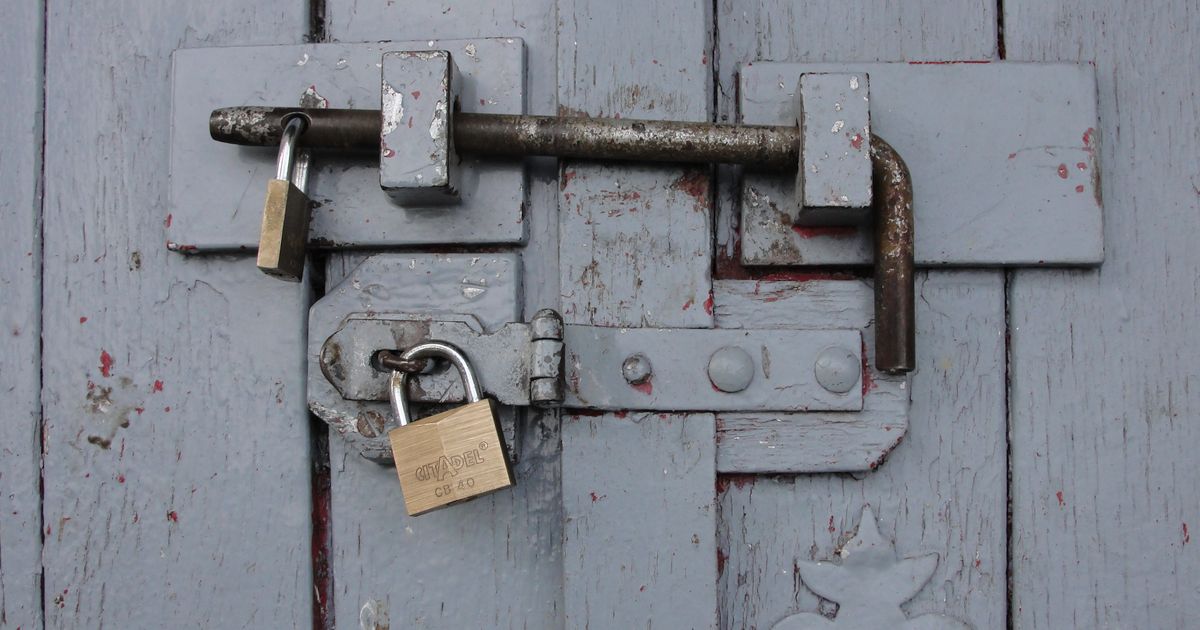 Detailed view of a securely locked wooden door with weathered brass padlocks