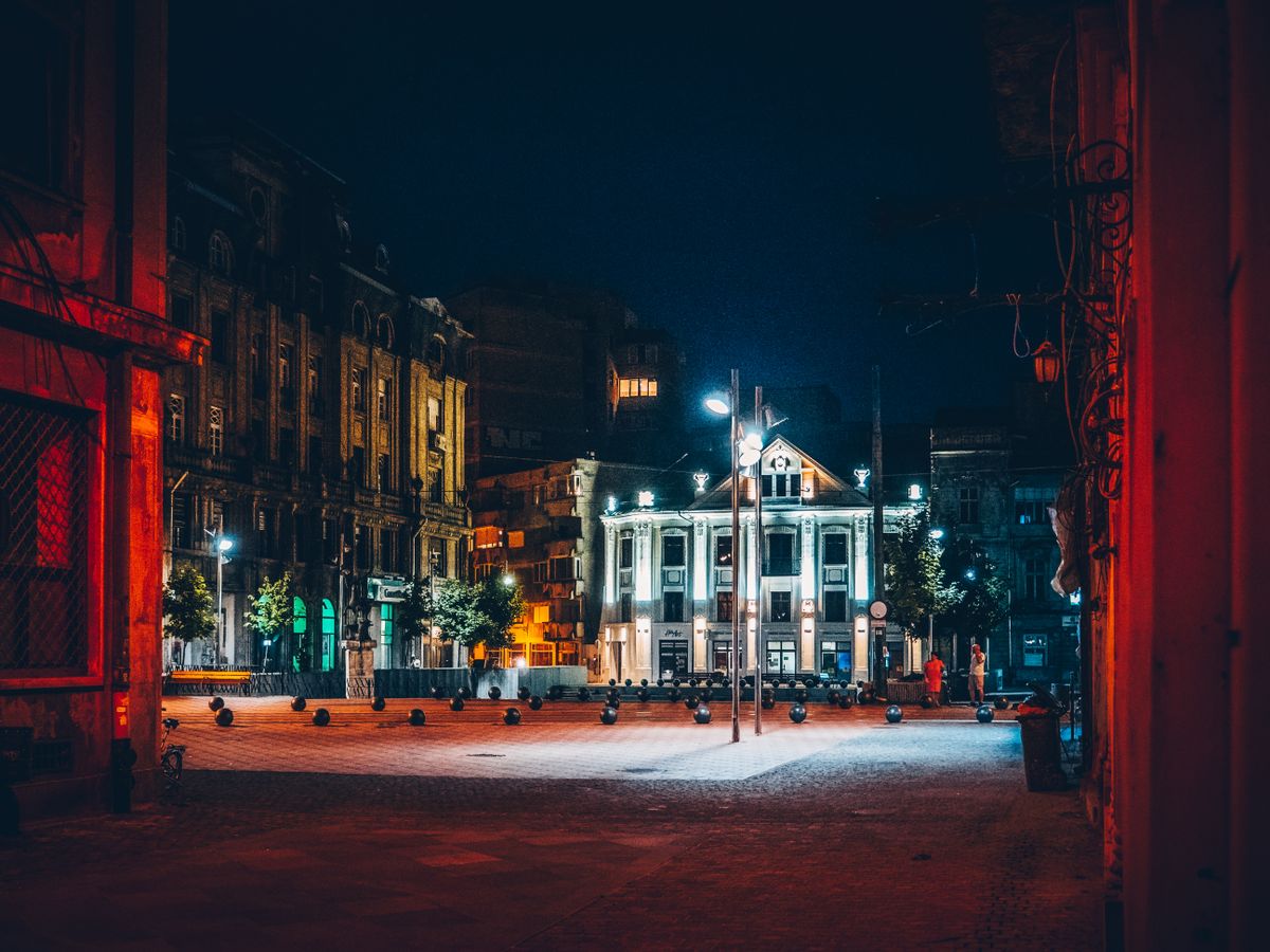 Piata istorica puternic iluminata seara, cu oameni pe pavaj