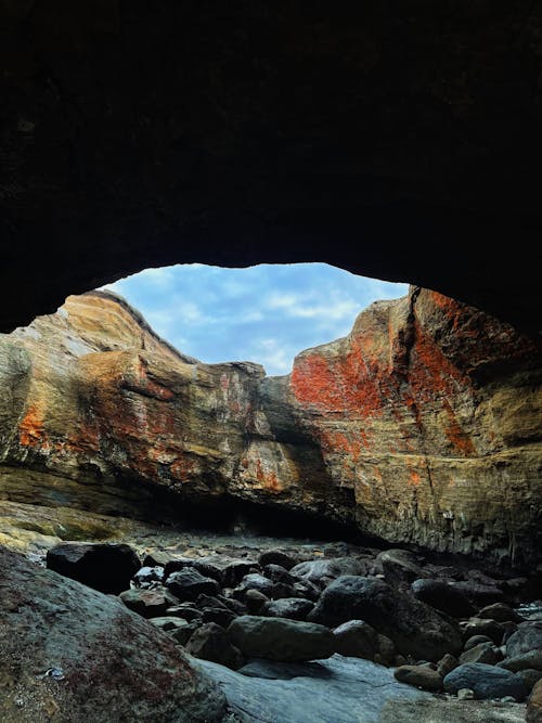 A Brown and Red Cliff Near a Cave with Gray Rocks 