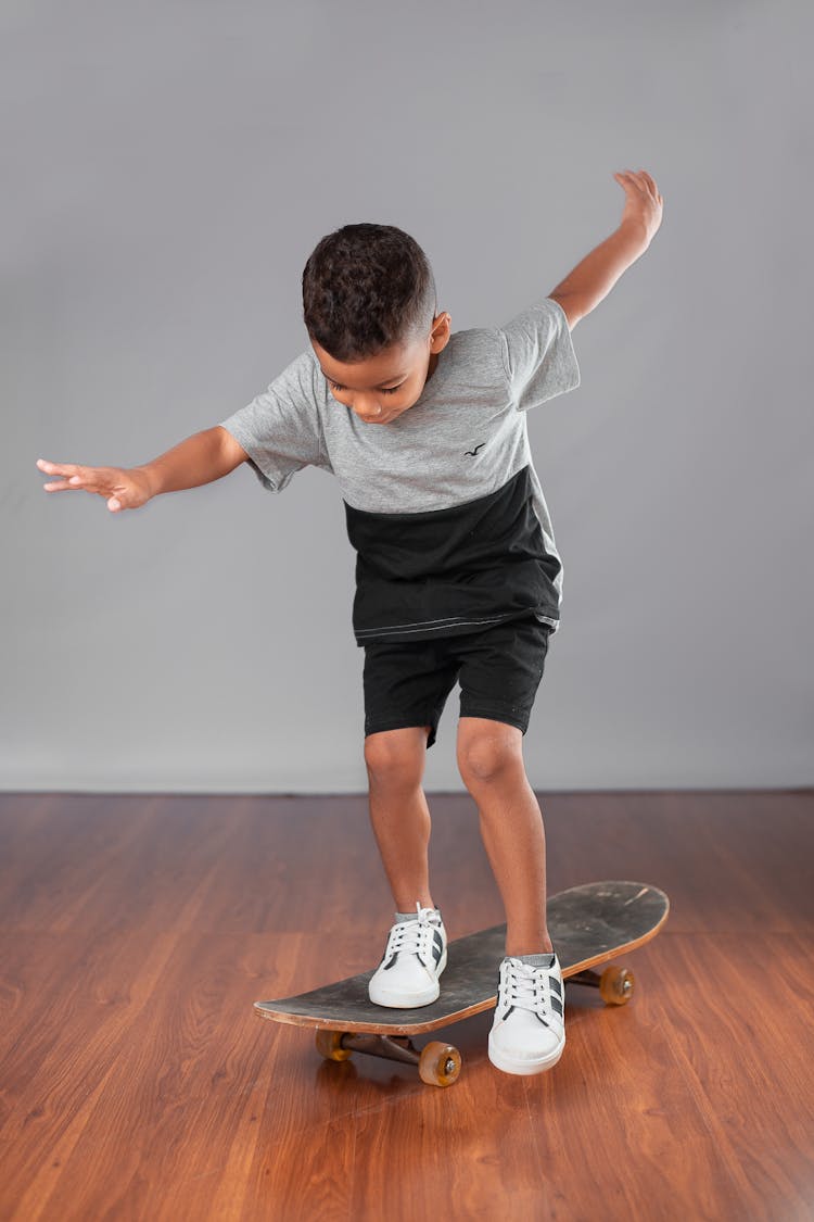 A Boy Wearing Gray Short And Black Shorts Standing On A Skateboard