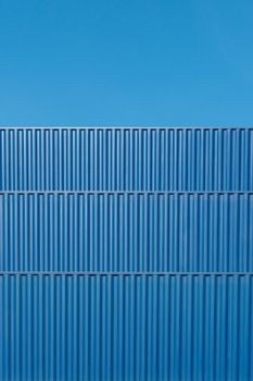 Minimalist view of blue corrugated shipping containers against a clear sky, capturing geometric patterns.