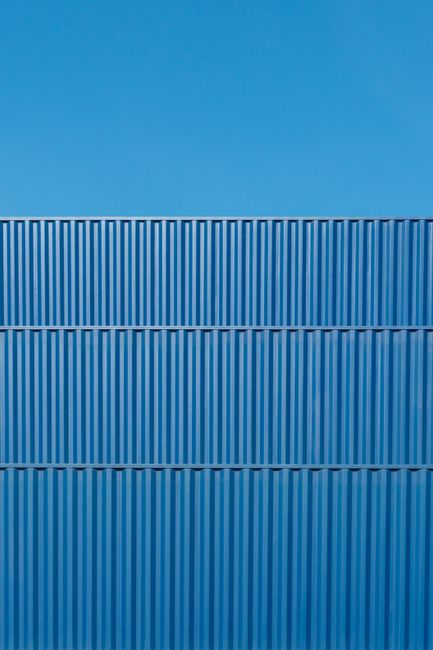Minimalist view of blue corrugated shipping containers against a clear sky, capturing geometric patterns.